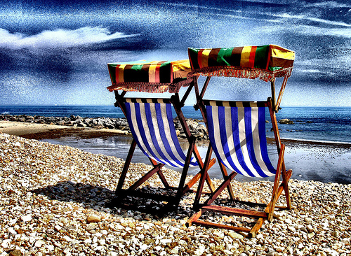 Two deck chairs on a beach.
